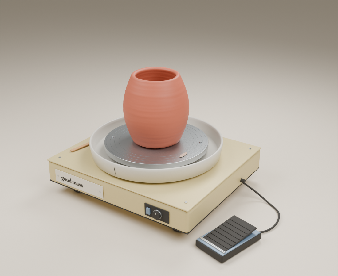 A terracotta pot on a warm cream Good Mess studio wheel, with a brushed aluminum wheelhead, removable splash pan, and ribbed rubber foot pedal.